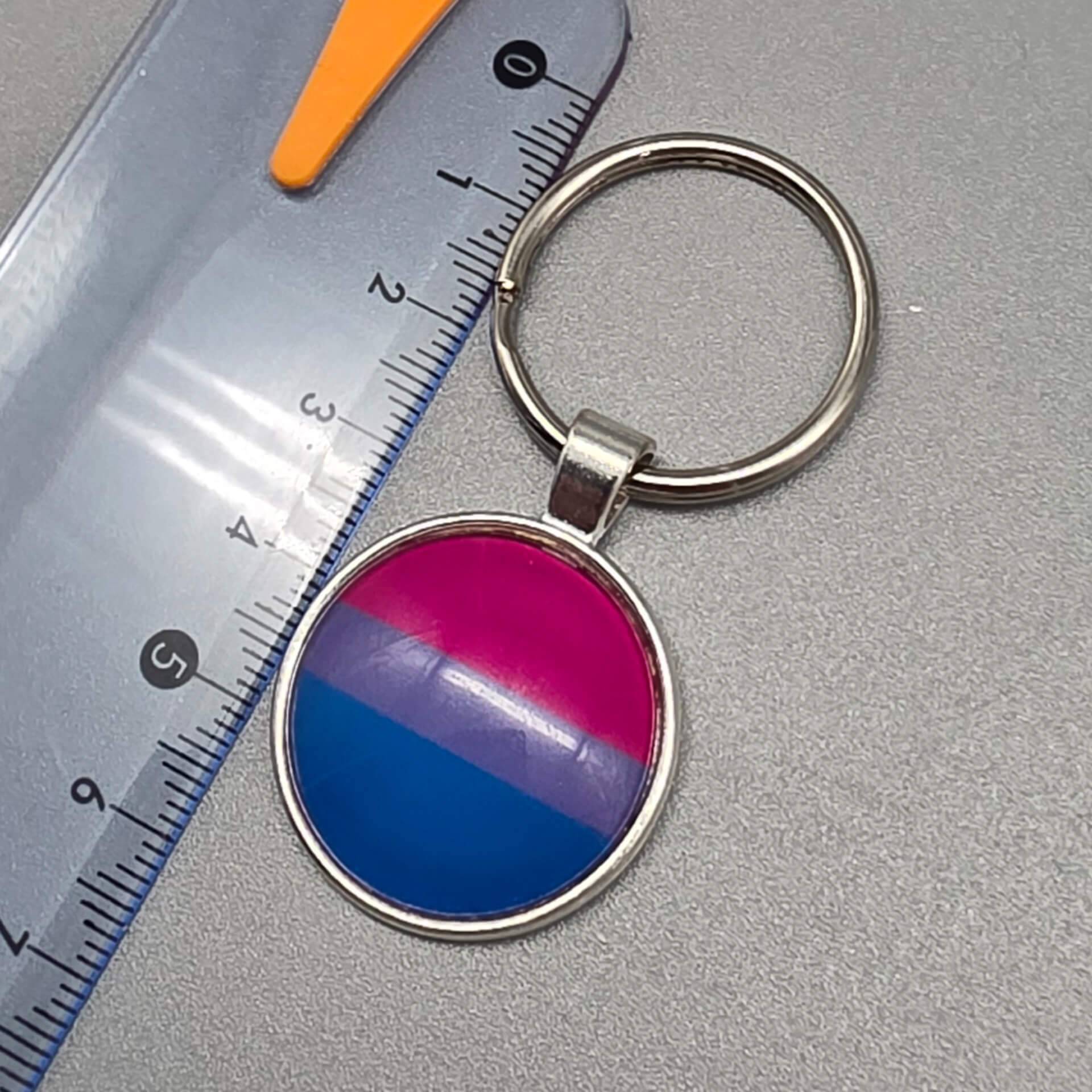 Silberner Bisexuell Schlüsselanhänger mit Bi Pride Flagge unter Glasdom, Nahaufnahme mit Lineal zur Darstellung der Größe