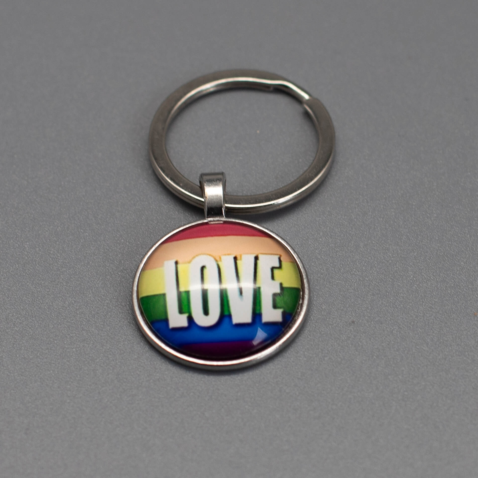 Silberner Pride Schlüsselanhänger mit Regenbogenfarben und großem weißem „LOVE“ Schriftzug unter gewölbtem Glasdom.