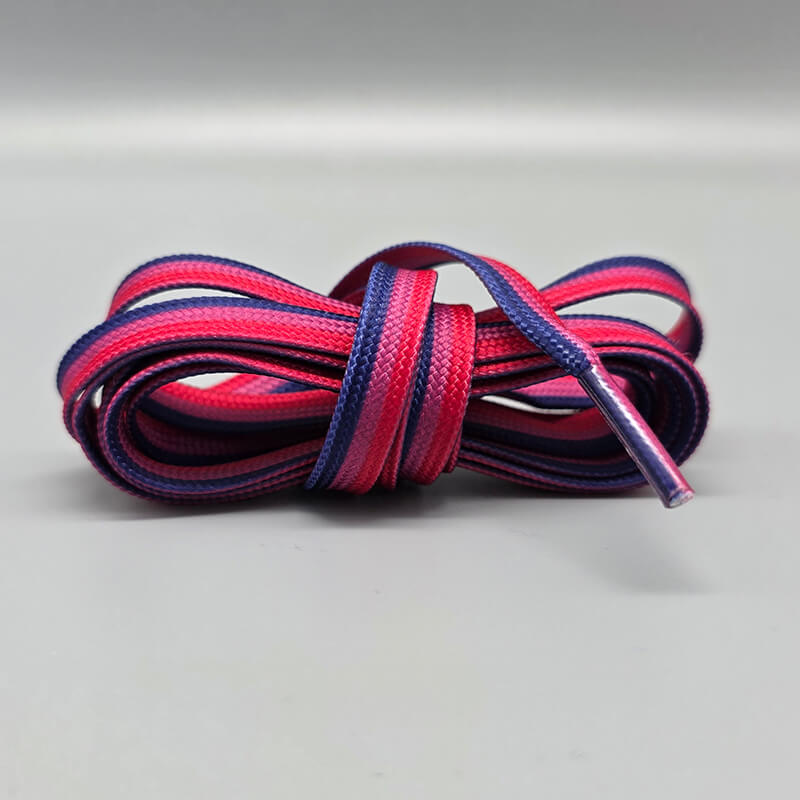 Ordentlich zusammengerollt präsentieren sich diese flachen Senkel in den drei charakteristischen Farben der bisexuellen Community. Die horizontalen Bahnen in Pink, Lila und Dunkelblau enden auf dem Studiofoto in einer transparenten Agraffe.
