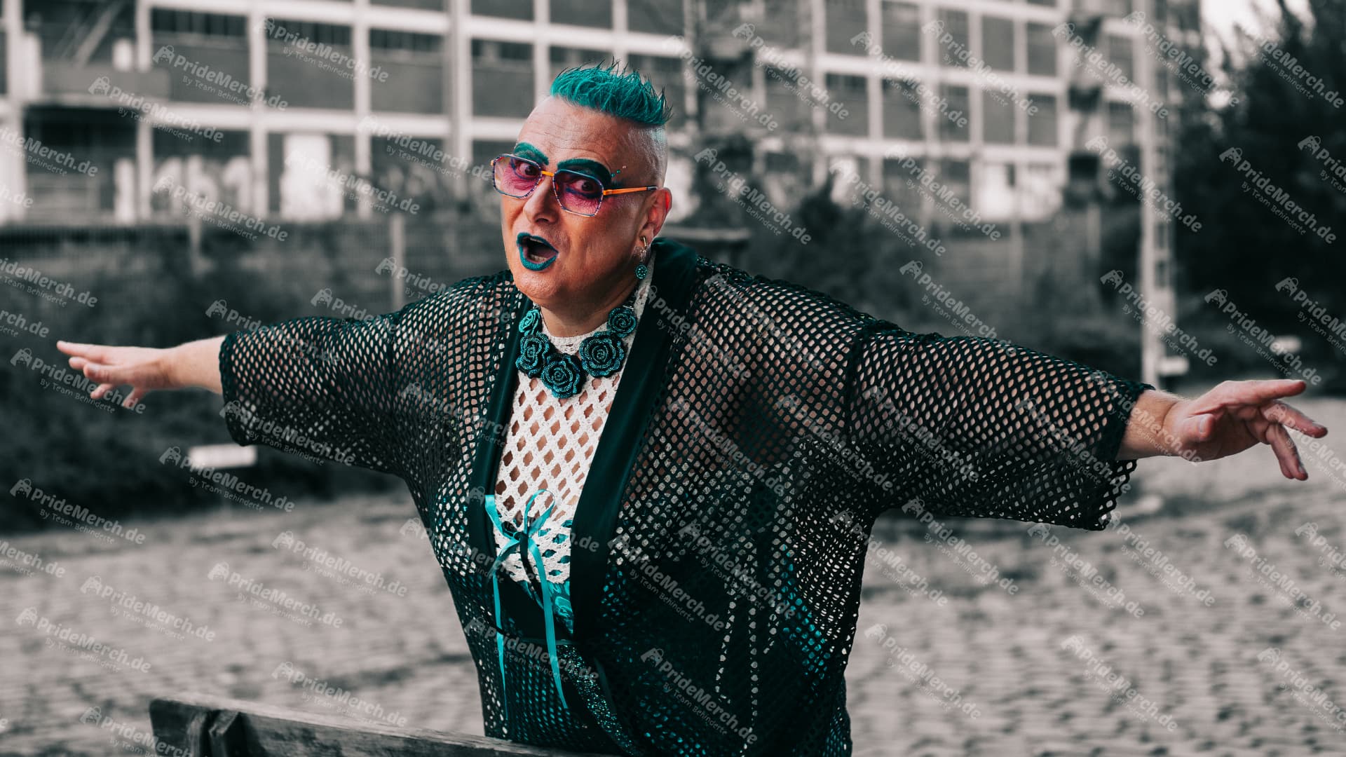 Das Bild "Ginatanic": Drag Queen Gina Petrolia posiert mit ausgebreiteten Armen in Anlehnung an den Film Titanic, gekleidet in einem Netz-Outfit mit türkisfarbenen Akzenten.