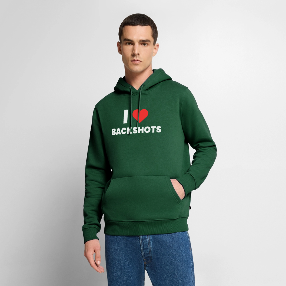Das Modell mit Vollbart trägt den flaschengrünen Kapuzenpulli in lässiger Pose. Die Kapuze des dicken Stoffes liegt locker auf den Schultern, während das humorvolle Pride-Design ein sex-positives Community-Statement setzt.