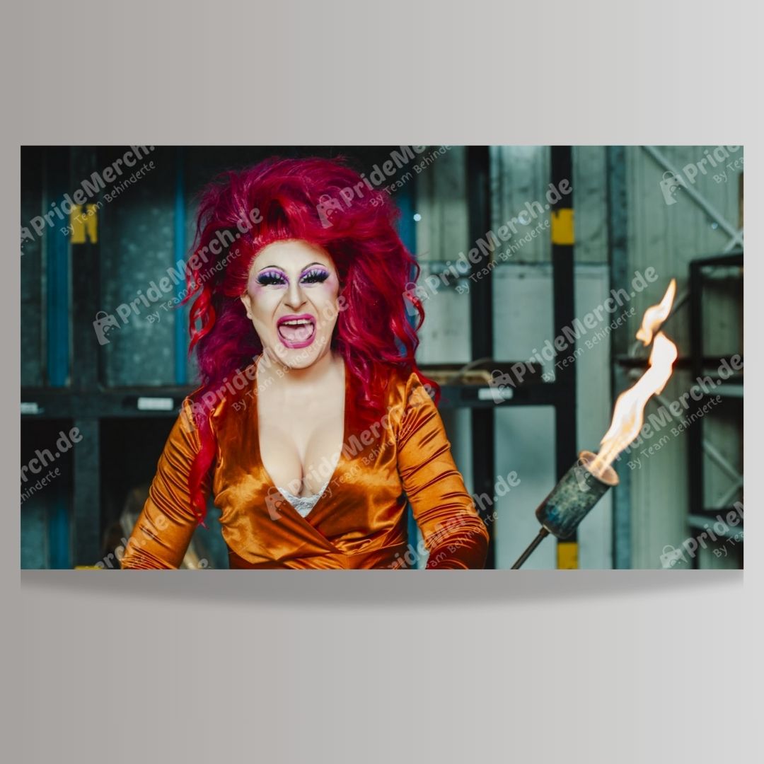Poster-Produktbild der Drag Queen Joyce DeLone aus Bremen. Sie trägt ein auffälliges, rotes, hochgestyltes Haar, dramatisches Make-up mit lila Lidschatten und pinken Lippen, und ein tief ausgeschnittenes, glänzendes orangefarbenes Kleid. Joyce hält einen Flammenwerfer-Requisit, aus dessen Düse eine lebendige Flamme schießt. Der Hintergrund wirkt industriell. Motivtitel: 'Flammenwerfer'. Verkauf über pridemerch.de by Team Behinderte.