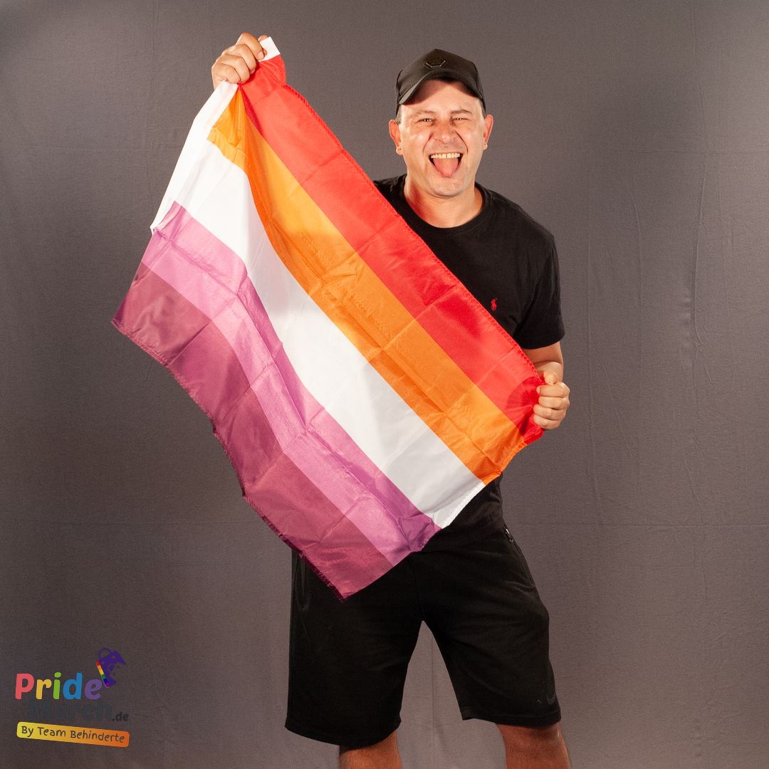 Ein lachender Mann hält die 90x60 cm große lesbische Flagge (Sunset-Variante) stolz in den Händen. Die Flagge ist ideal für CSD-Events und Pride-Partys.