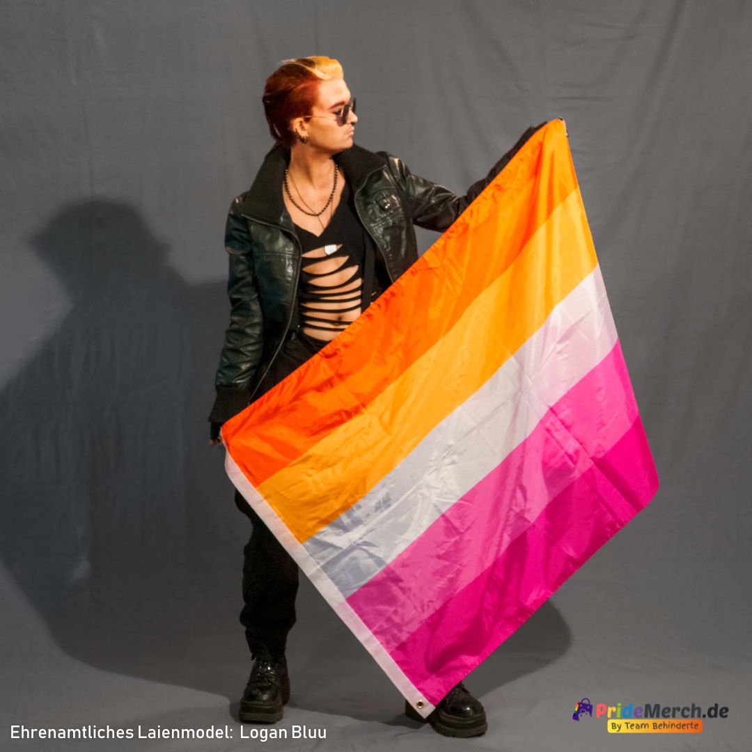 Eine Person (Logan Bluu) hält die große lesbische Sunset-Flagge aus Polyester ausgebreitet vor sich. Die 150x90 cm Flagge zeigt die leuchtenden 5 Farben und die Metall-Ösen an der Ecke.