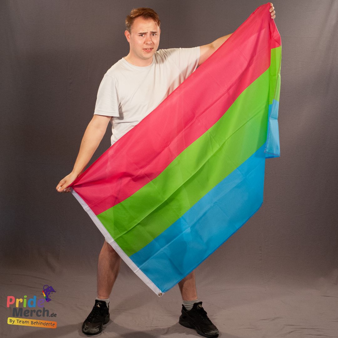 Das ehrenamtliche Laienmodell Luna (Drag Queen aus Bremen) hält die polysexuelle Pride-Flagge mit ausgestrecktem Arm im Fotostudio. Die Bewegung zeigt die Leichtigkeit des Polyester-Stoffs.
