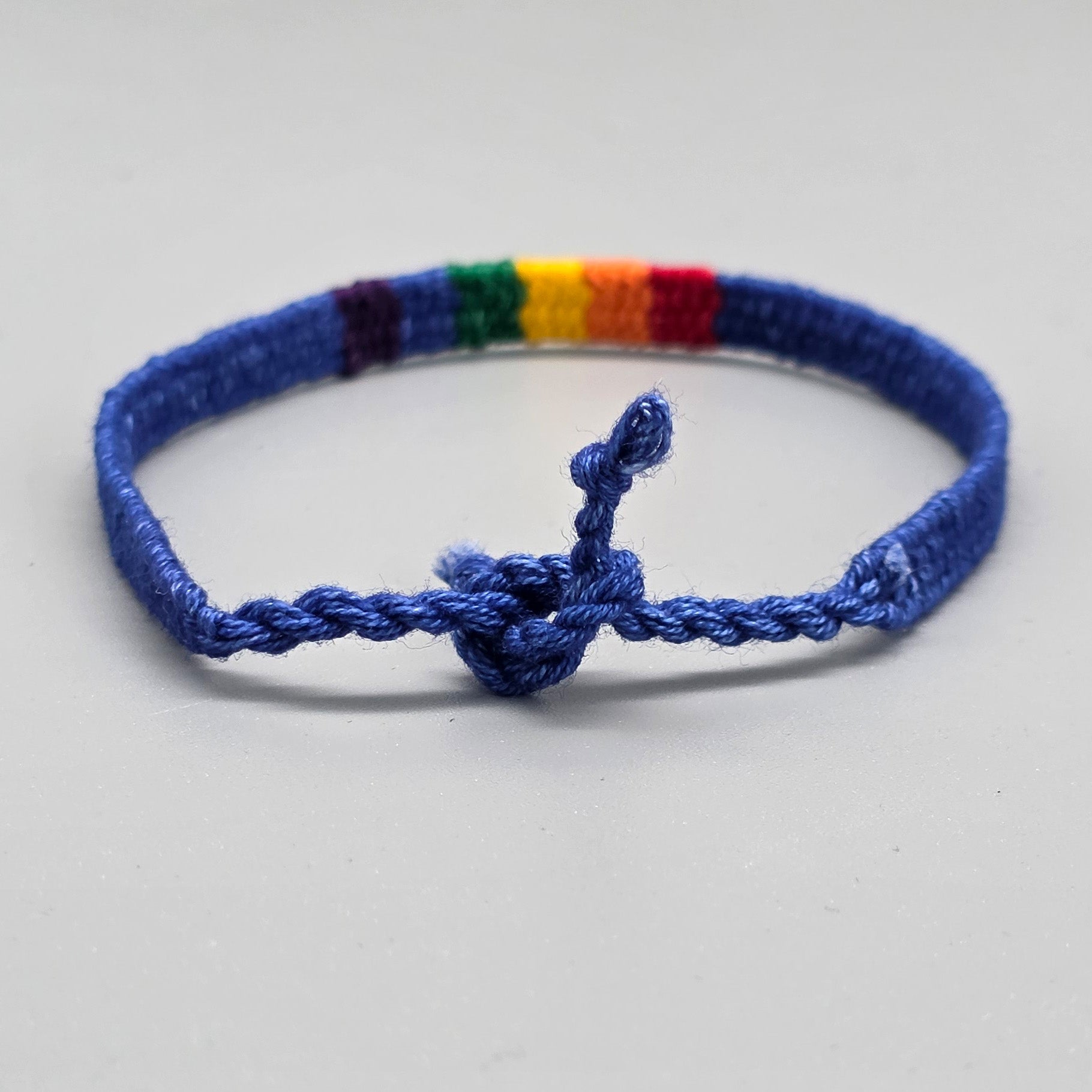 Die Rückansicht des ozeanblauen Baumwollbändchens zeigt die geflochtene Struktur im Detail. Der handgeknüpfte Schiebeknoten verbindet die beiden Kordelenden und veranschaulicht die flexible Größenverstellbarkeit des queeren Schmuckstücks.
