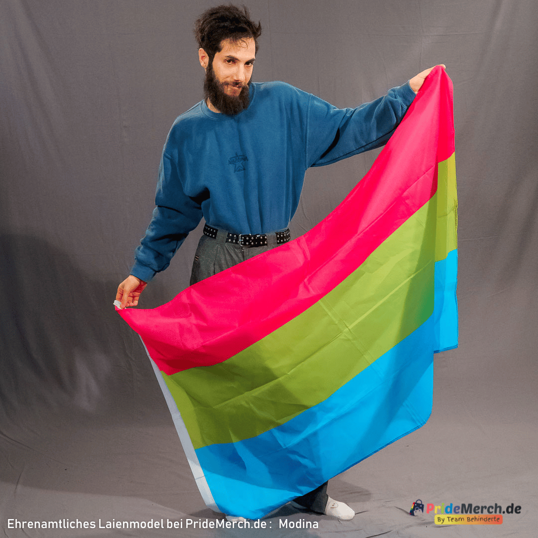 Laienmodell Modina hält die polysexuelle Flagge im Studio aufrecht vor dem Körper. Die 150x90 cm große Polyesterfahne zeigt die klare Aufteilung der Streifen in Pink, Grün und Blau.