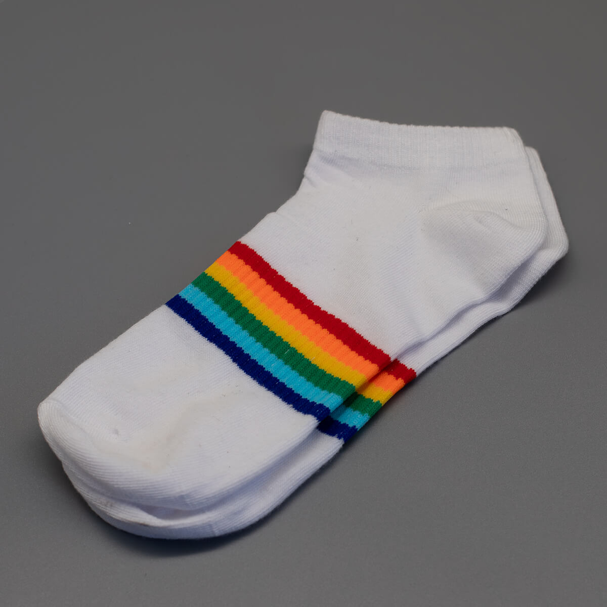 Zentral über den Mittelfuß verlaufen die farbintensiven Nuancen der LGBTQ-Bewegung bei diesem reinweißen Paar Socken. Die freigestellte Produktansicht verdeutlicht das cleane Design, das sich optimal für sommerliche Pride-Events eignet.