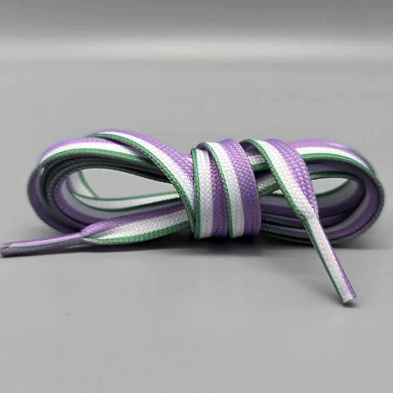 Ein Paar aufgerollte Pride-Schnürsenkel in den Farben der Genderqueer-Flagge. Die flachen Schnürsenkel haben Längsstreifen in Lavendel, Weiß und Grün und liegen auf einem neutralen, grauen Hintergrund.