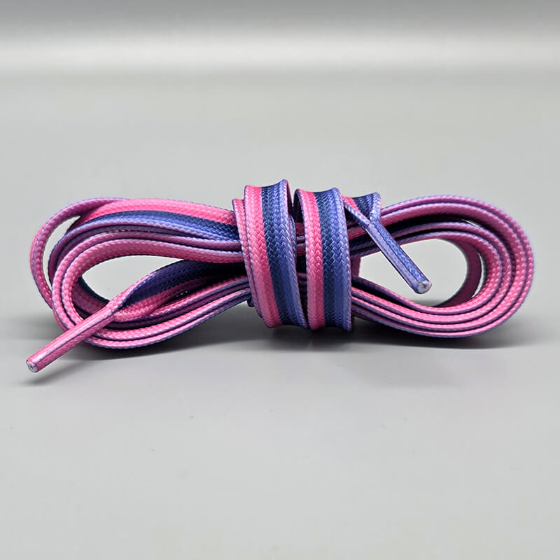 Ein Paar Schnürsenkel, gebündelt auf einem hellgrauen Hintergrund. Die Schnürsenkel zeigen das Farbschema der omnisexuellen Flagge mit horizontalen Streifen in leuchtendem Pink, Lila und einem dunkleren Blau/Violett. Die Schnürsenkelenden (Agletten) sind farblich passend.