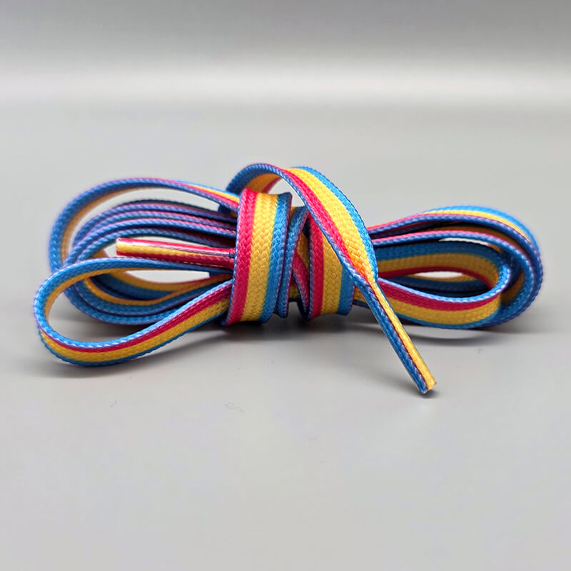 Nahaufnahme eines flachen Schnürsenkels mit parallelen Streifen in den Farben der pansexuellen Flagge (Pink, Gelb, Blau). Der Schnürsenkel ist zu einer lockeren Schleife gelegt und liegt auf einem glatten, hellgrauen Hintergrund.