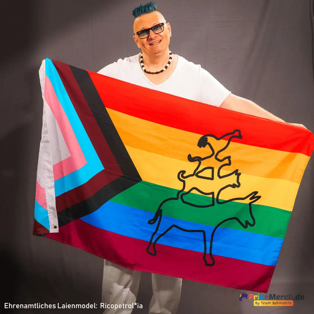 Das ehrenamtliche Laienmodel Ricopetrol*ia präsentiert stolz die großformatige Bremer Stadtmusikanten Progress Pride Flagge. Das Bild zeigt deutlich das Verhältnis der Flagge zur Körpergröße und die intensiven Farben des Designs.