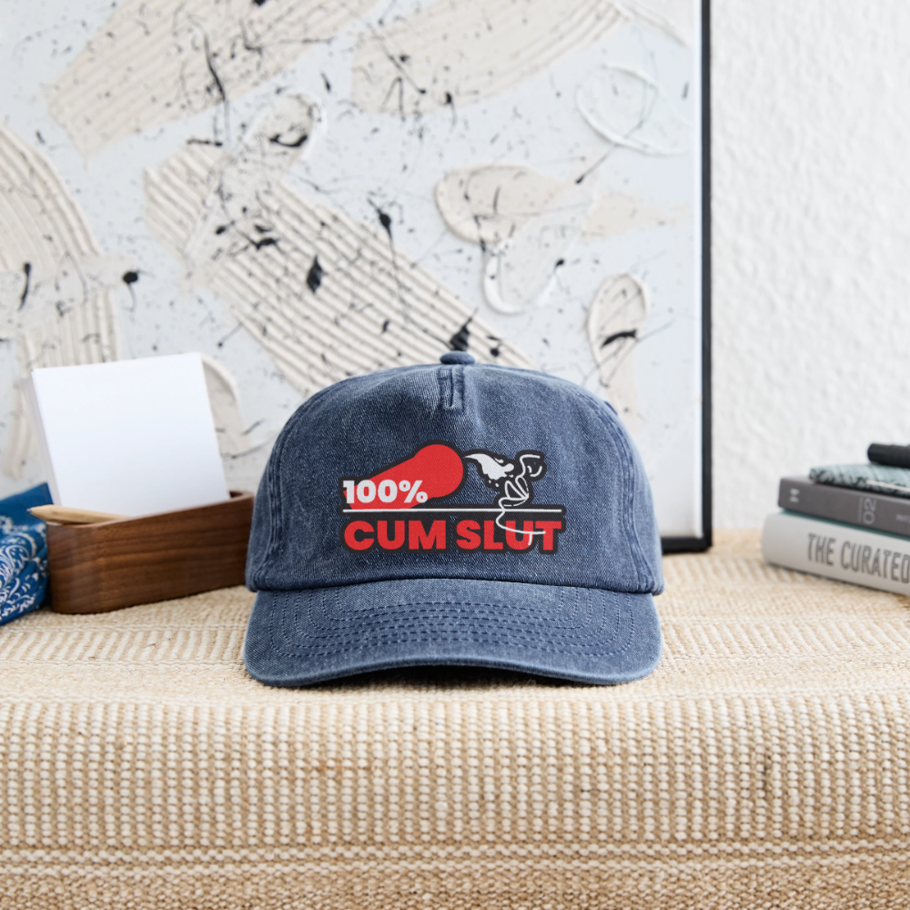 Vintage Denim Cap mit dem frechen "100% Cum Slut" Kink Fetish Design liegt auf einer Garderobenablage – klares Statement für devote Bottoms und Twinks, die ihre devote Rolle bei CSD, Pride und Clubnächten offen zeigen