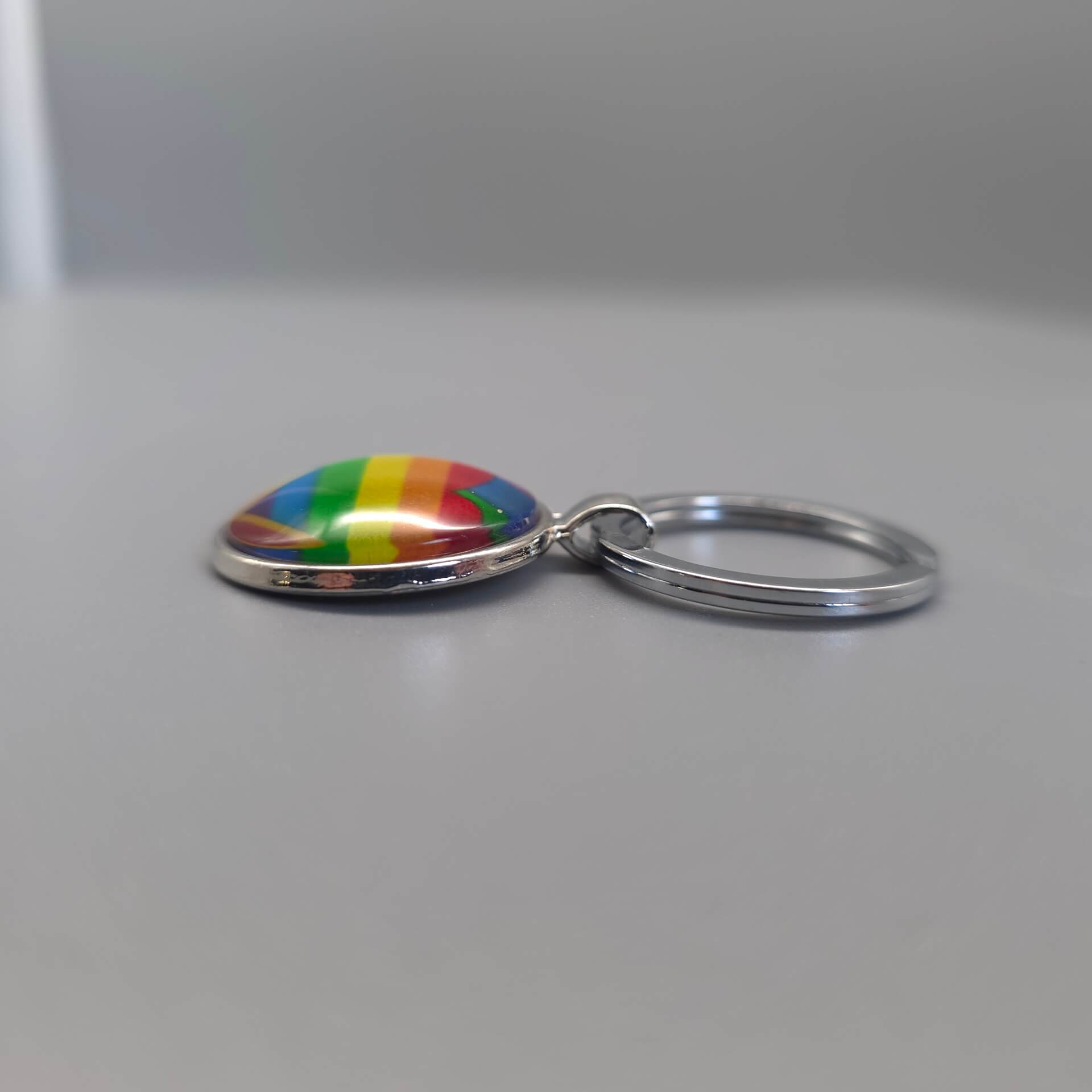 Seitenansicht eines Pride Schlüsselanhängers mit gewölbtem Glasdom, sichtbar erhöhter Oberfläche und Regenbogen Herz Motiv.