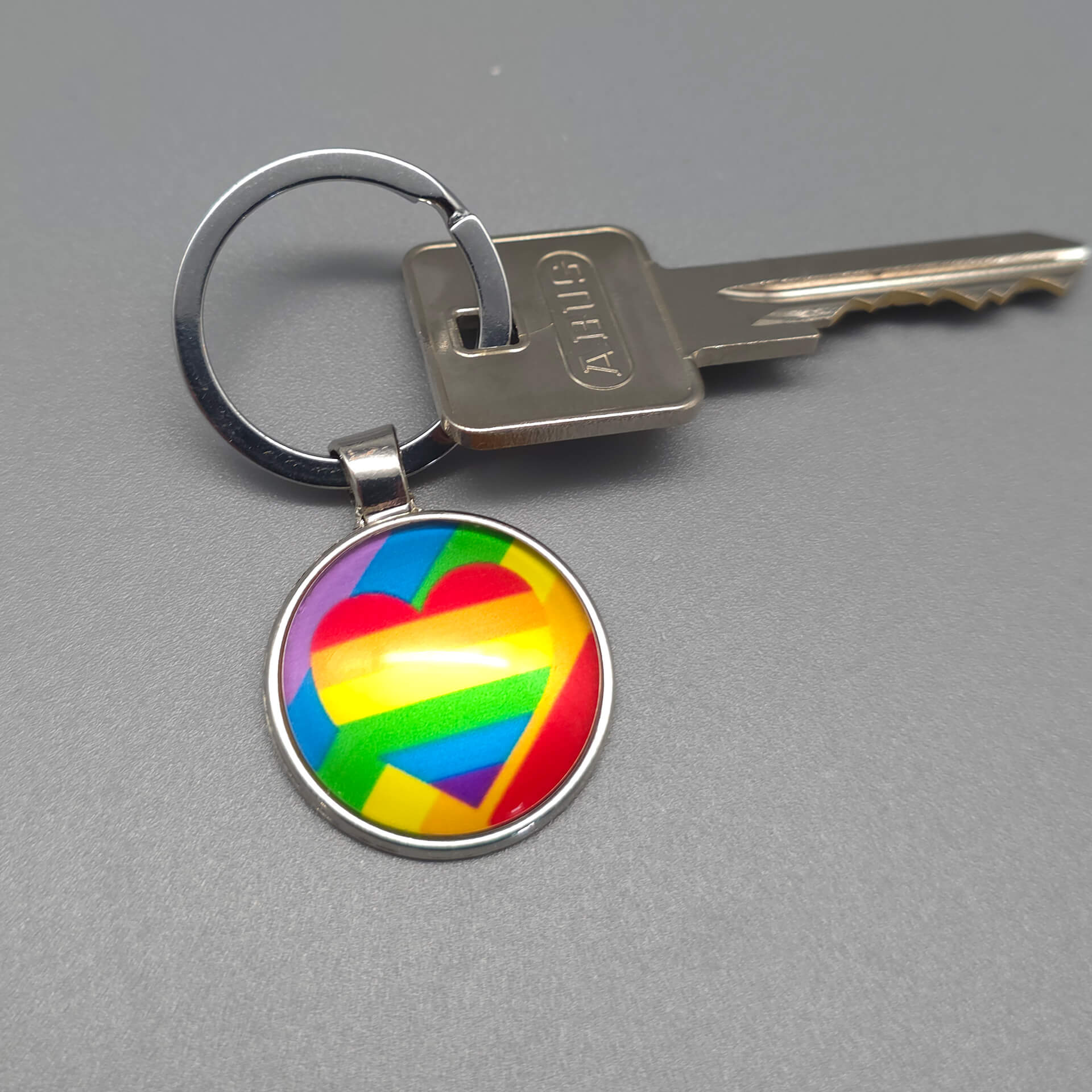 Pride Schlüsselanhänger in Silber mit einem bunten Regenbogen Herz Motiv unter einem gewölbten Glasdom.