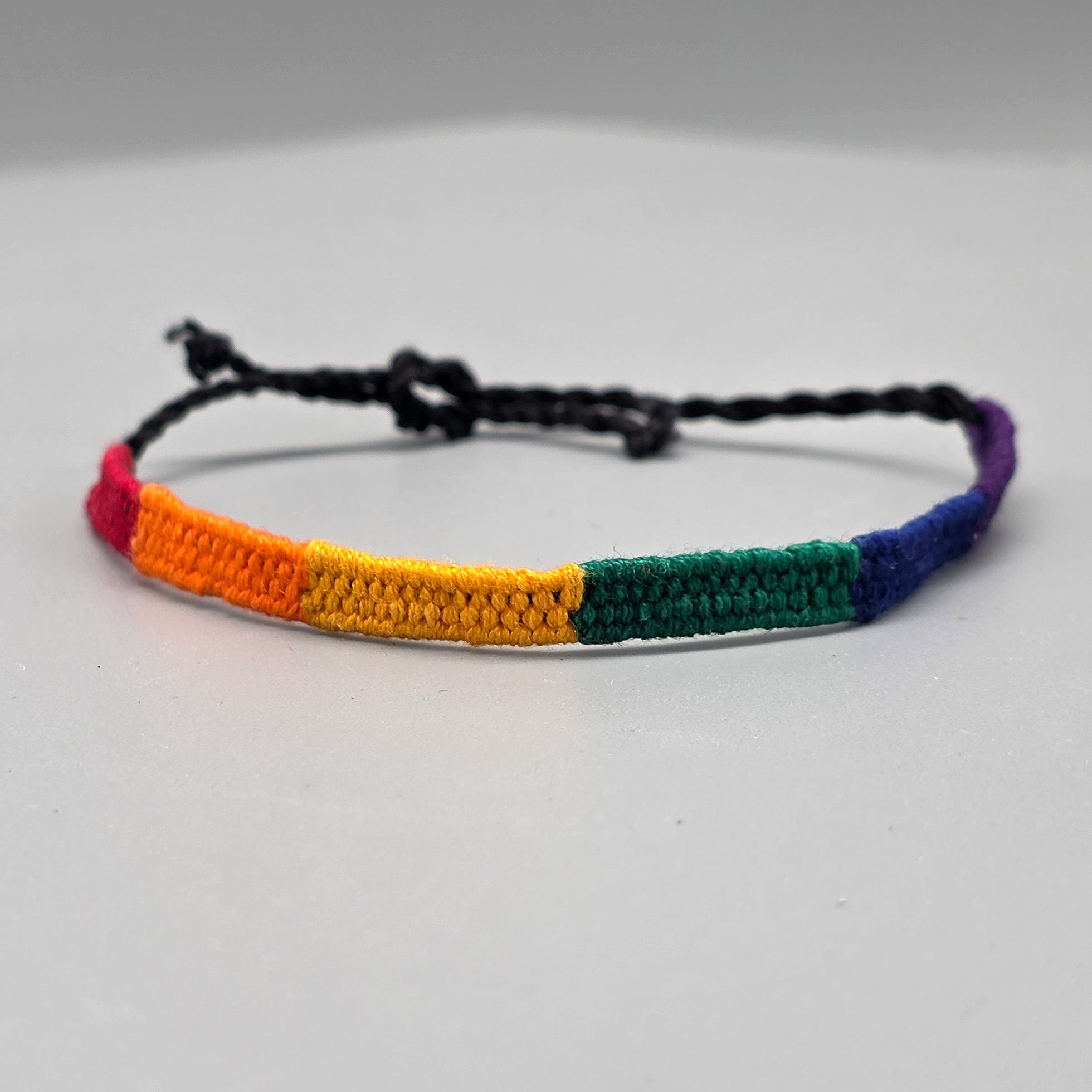 Aus rechter Perspektive zeigt sich das farbintensive Macramé-Armband auf der neutralen Studiofläche. Im Fokus stehen die sauber verarbeiteten, dunkelblauen und lila Abschnitte, die direkt in das schwarze Befestigungsband übergehen.