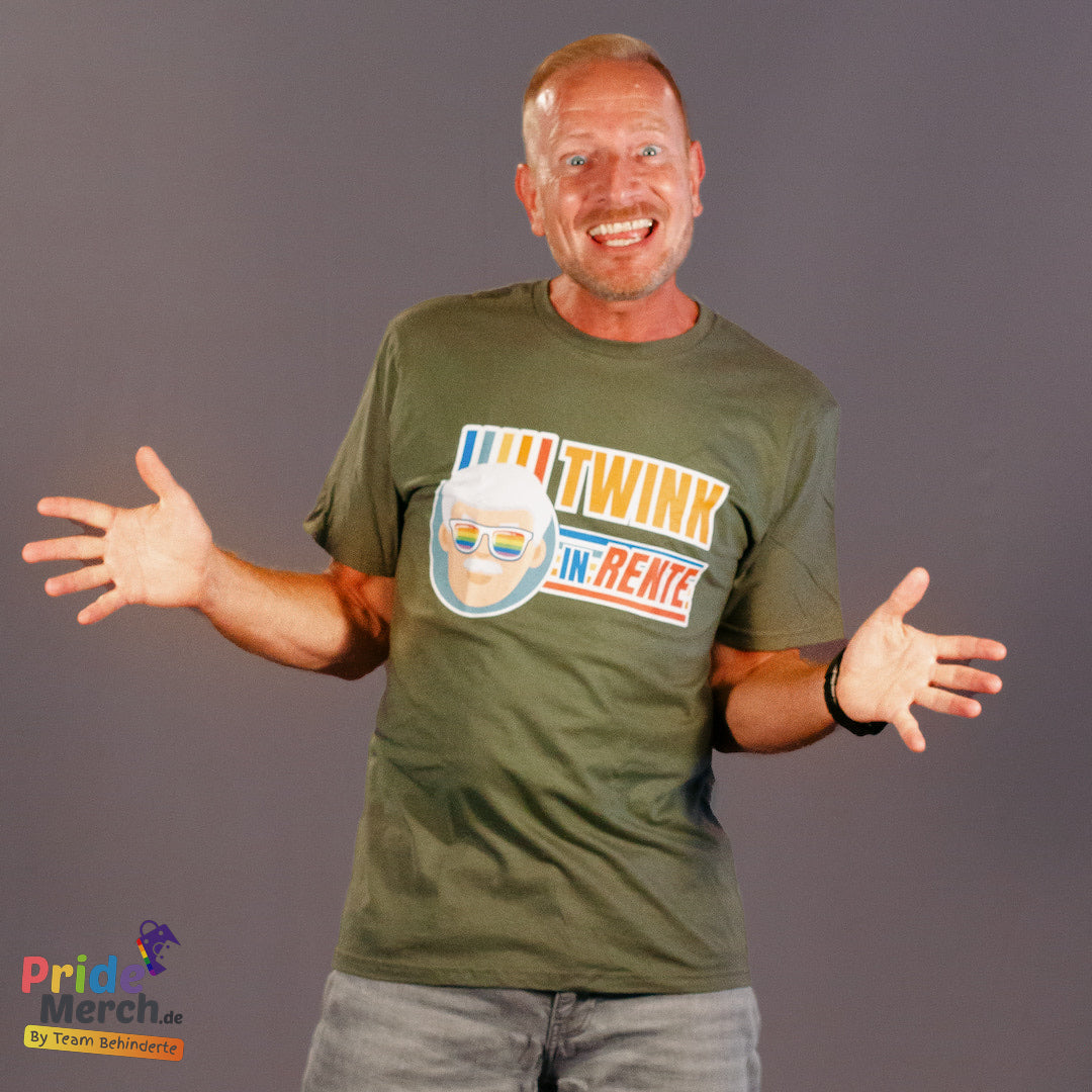 „Mann mit lächelndem Gesicht und ausgestreckten Armen trägt ein olivgrünes T-Shirt mit dem PrideLab-Design 'Twink in Rente'. Das Design zeigt eine stilisierte Abbildung eines älteren Mannes mit weißem Haar und Regenbogen-Sonnenbrille sowie den Text 'TWINK IN RENTE' in bunten, lebendigen Farben. Das Shirt wird von PrideMerch.de präsentiert – einem Online-Shop für LGBTQ+-Merchandise, der von Team Behinderte betrieben wird. Der humorvolle und stolze Look verbindet Pride-Kultur mit spielerischer Selbstironie.