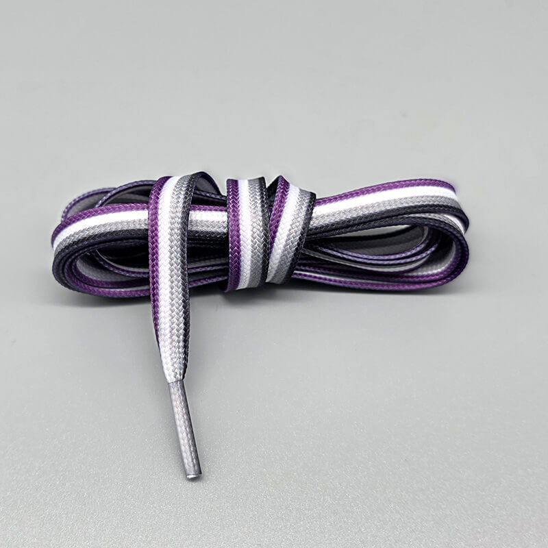 Locker zu einer Schleife gebunden ist dieses Paar flacher Pride-Schnürsenkel in der asexuellen Ausführung. Das Stoffmuster setzt sich aus vier horizontalen Streifen in Dunkellila, Lavendel, Hellgrau und Weiß zusammen.