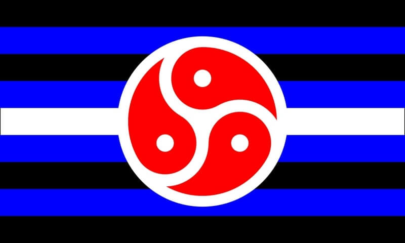 Die BDSM-Flagge als flache Grafikdarstellung. Das Motiv zeigt horizontale Streifen in Schwarz, Blau, Schwarz, Weiß, Schwarz, Blau, Schwarz. Im Zentrum des weißen Streifens liegt ein markantes rotes Triskelion auf einem weißen Kreis, das sofort ins Auge fällt.