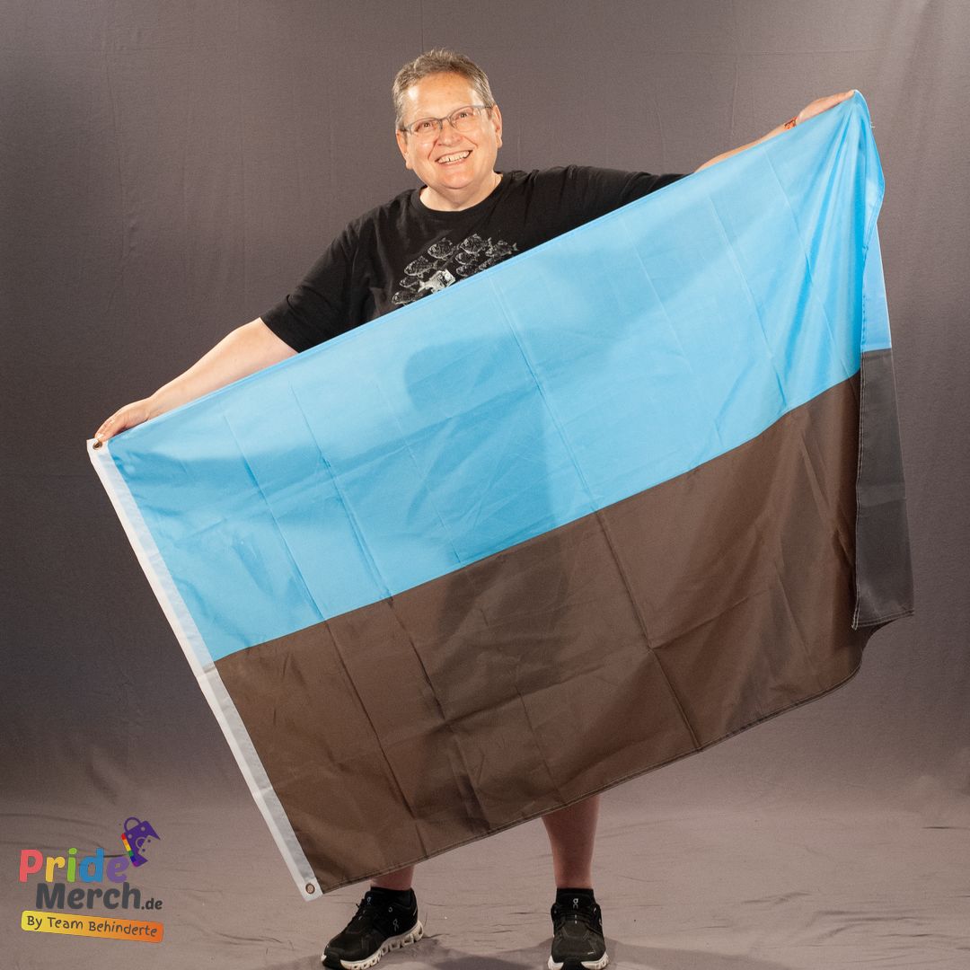 Das ehrenamtliche Laienmodell Beate Pellegrino hält die 150x90 cm große autosexuelle Pride-Flagge mit ausgebreiteten Armen lächelnd im Fotostudio. Die hellblaue und graue Aufteilung der Polyesterfahne ist im vollen Format sichtbar.