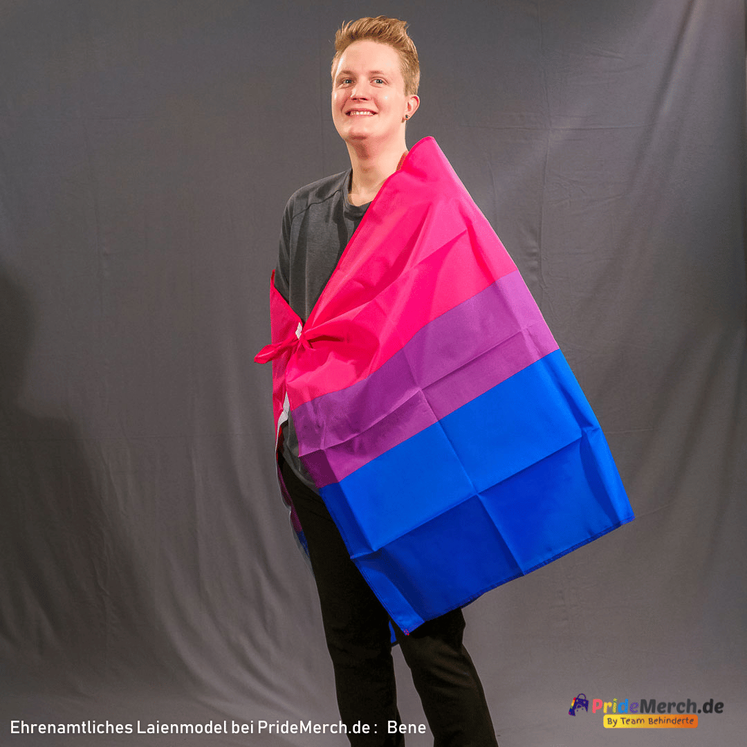 Ehrenamtliches Laienmodel Bene präsentiert die große Bisexuell-Flagge (150x90 cm), die wie ein Cape um die Schultern geknotet ist. Die kräftigen Streifen in Pink, Lila und Blau symbolisieren Bi-Sichtbarkeit und Stolz.