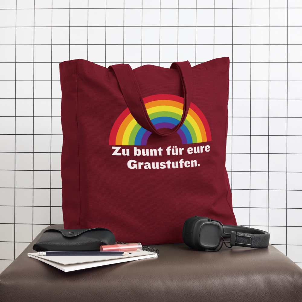Burgunderrote Pride Tragetasche im Lifestyle-Look auf einem Lederhocker, daneben Kopfhörer und Notizbuch
