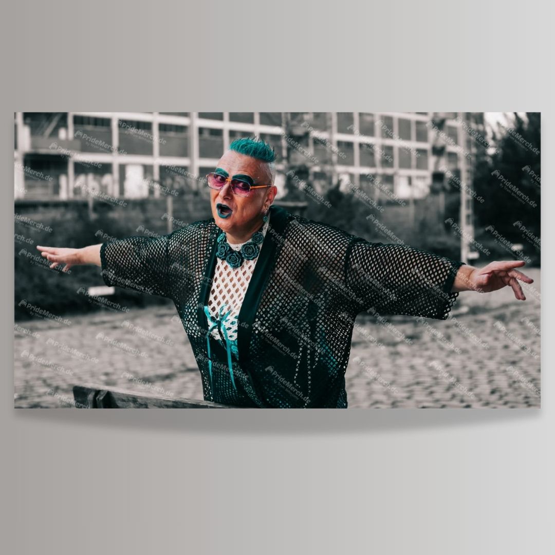 Poster-Produktbild der Drag Queen Gina Petrolia. Sie hat kurzes, leuchtend türkisfarbenes Haar, trägt eine auffällige, rosa getönte Brille und dunkle Lippenstift. Ihr Outfit besteht aus einem schwarzen, durchsichtigen Netz-Kimono über einem weißen, gemusterten Unterteil, kombiniert mit einer großen, türkisfarbenen Blumen-Halskette. Gina steht mit weit ausgestreckten Armen in einer expressiven, offenen Pose, als würde sie singen oder rufen. Der Hintergrund zeigt ein verlassenes, vergrautes Gebäude in monochr