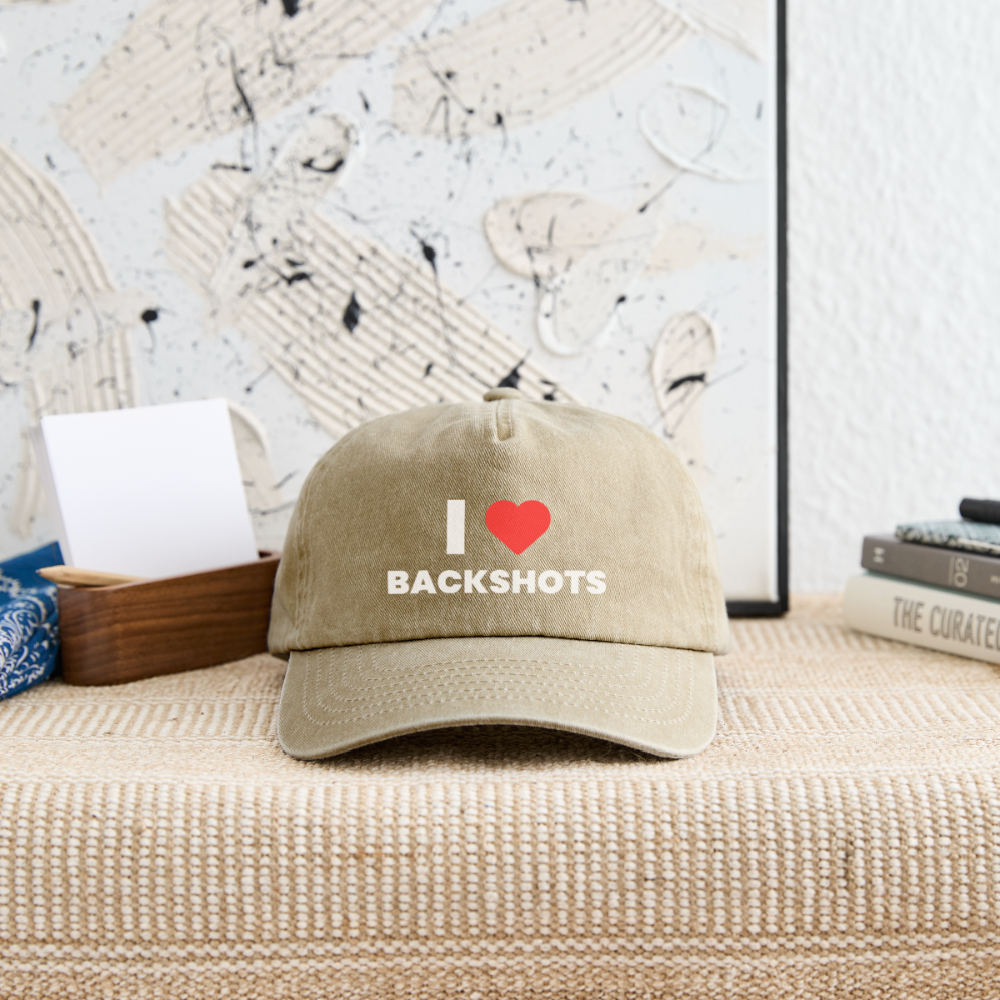 Blick auf die beige Vintage-Cap, die locker auf einem hellen Tisch abgelegt ist. Das zentrierte rote Herz-Meme von PrideMerch bricht den schlichten Look der Kopfbedeckung mit einem selbstbewussten, kinky Augenzwinkern.