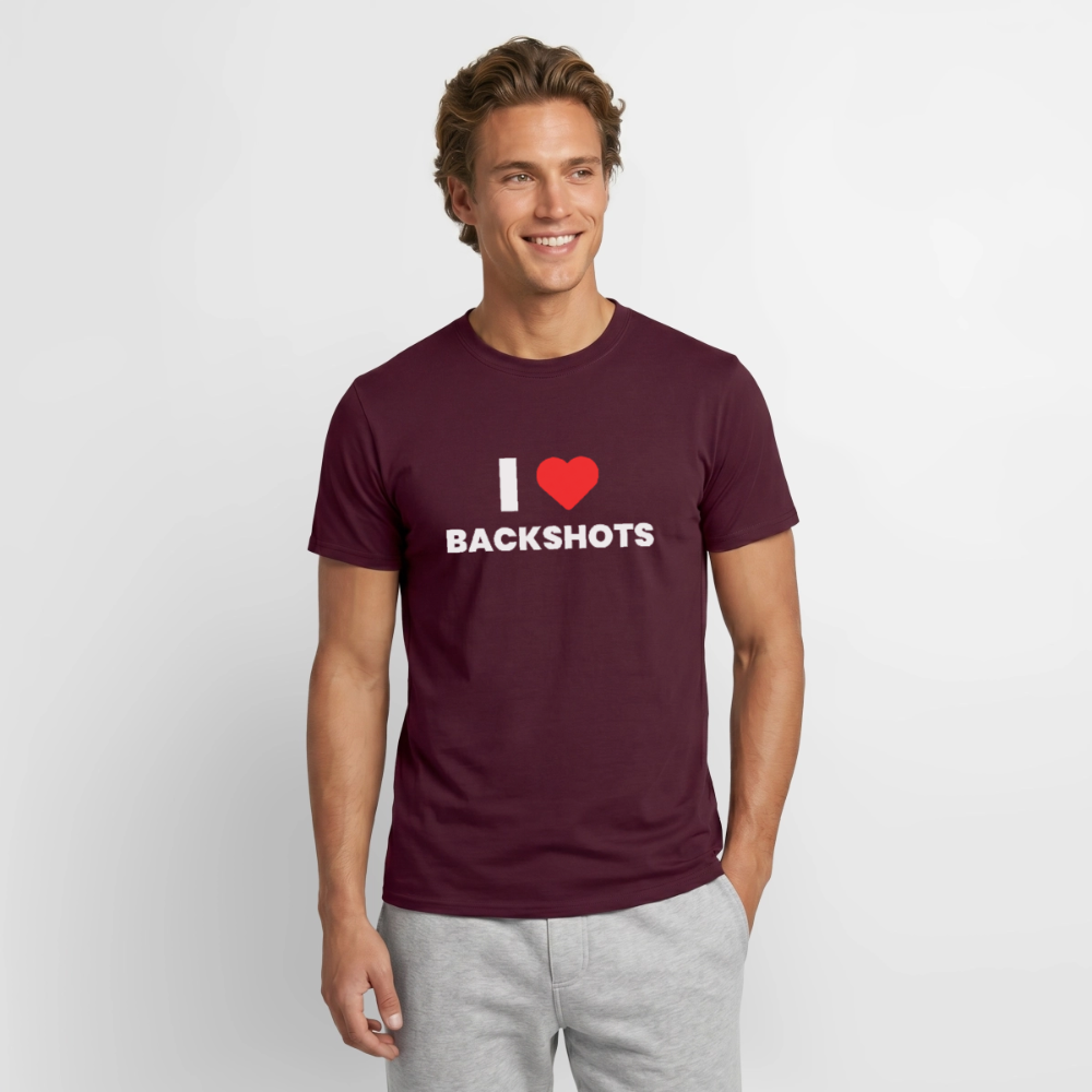 Das Modell mit Vollbart trägt das ziegelrote T-Shirt mit der Aufschrift „I ❤️ BACKSHOTS“. Ein ironisches Kleidungsstück, das queeren Humor und sex-positive Sichtbarkeit perfekt miteinander verbindet.