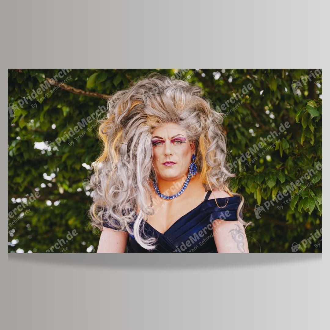  Poster der Drag Queen Jolina Wings als "Gartenkönigin". Sie trägt eine voluminöse, grau-blonde Perücke und blickt mit ernstem Ausdruck vor einem Hintergrund aus grünen Blättern direkt in die Kamera. Verkauf über pridemerch.de by Team Behinderte
