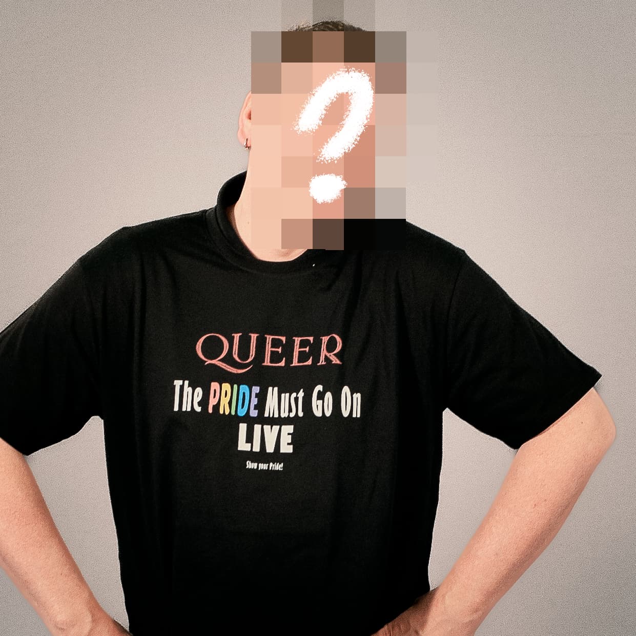 Der Künstler hinter der Drag Queen Jolina Wings, dessen Gesicht unkenntlich gemacht ist, trägt ein schwarzes T-Shirt mit dem bunten Aufdruck "QUEER The PRIDE Must Go On LIVE"