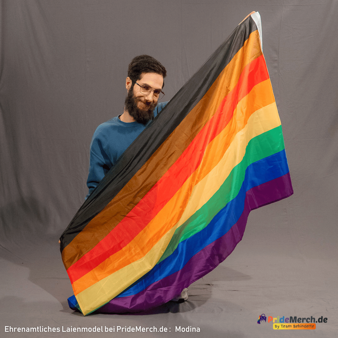 Das ehrenamtliche Modell Modina präsentiert lächelnd in kniender Pose im Fotostudio die Philadelphia Pride-Fahne. Die Bewegung zeigt den weichen Faltenwurf des leichten Polyesterstoffs.