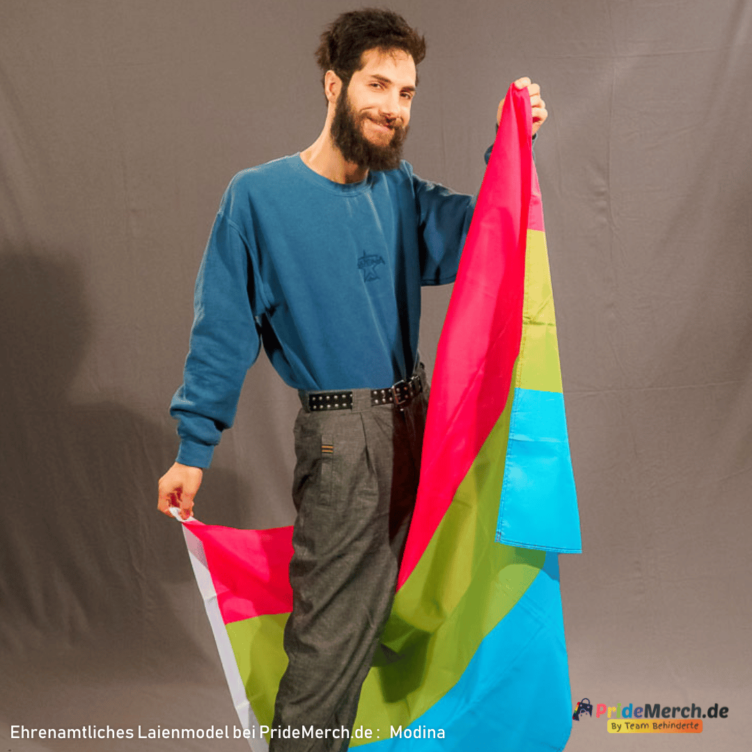 Das ehrenamtliche Laienmodell Modina posiert lächelnd im Fotostudio und hält die dreifarbige polysexuelle Pride-Flagge dynamisch an den Kanten hoch, sodass die Farben Pink, Grün und Blau im Faltenwurf gut zur Geltung kommen.