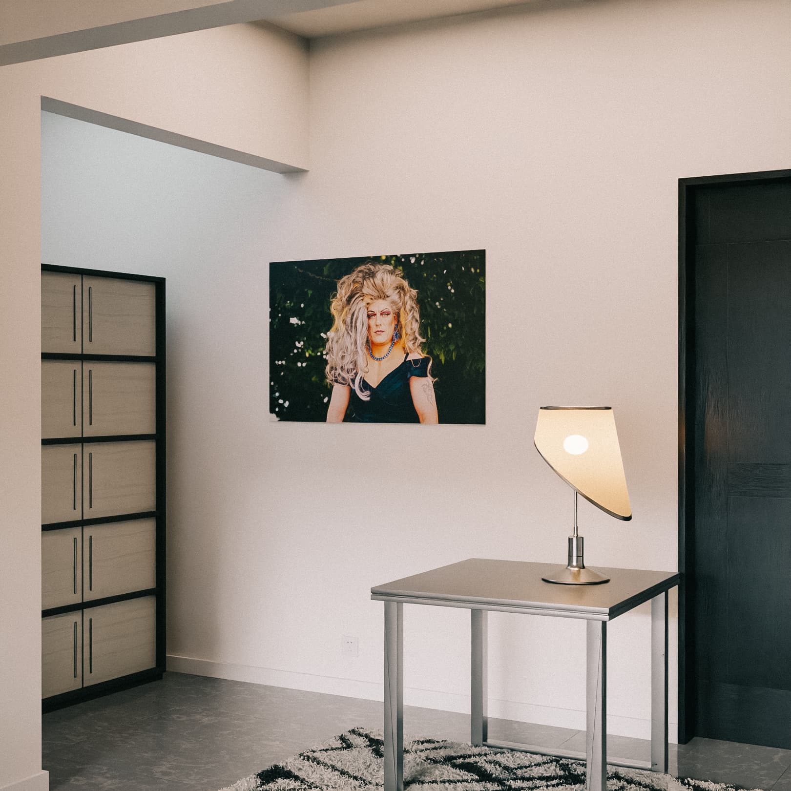 Mockup-Bild des "Gartenkönigin"-Posters. Das Porträt der Drag Queen Jolina Wings mit großer grauer Perücke hängt in einem modern eingerichteten Raum.