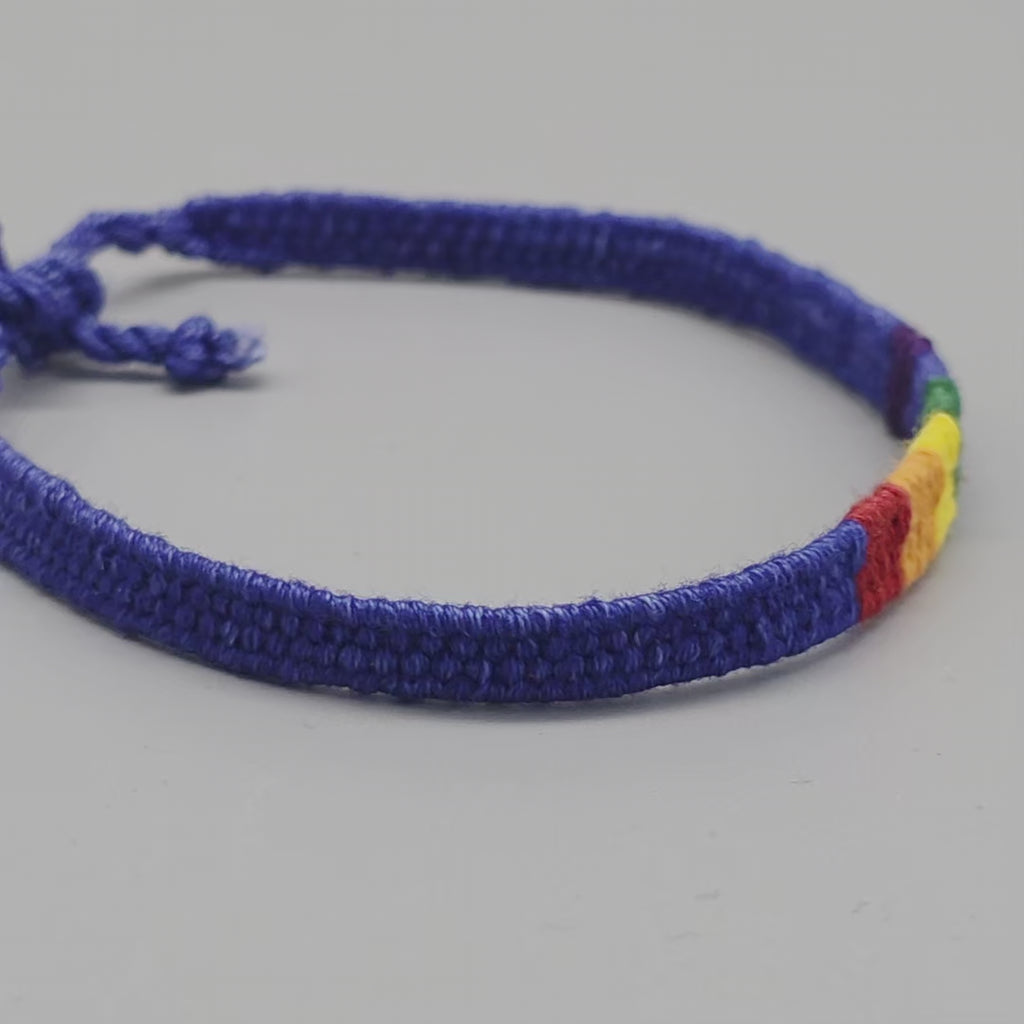 360-Grad-Produktvideo der handgewebten Pride-Freundschaftsarmbänder. Zu sehen sind nacheinander die ozeanblaue Variante mit Regenbogen-Akzent, das Allover-Regenbogenband mit schwarzer Kordel sowie der handgeknüpfte Schiebeknoten-Verschluss aus Baumwolle.