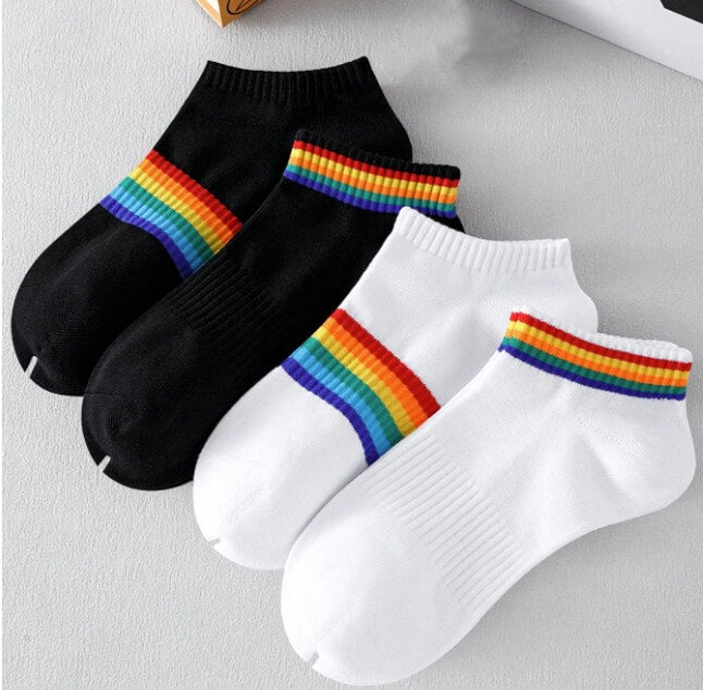 Vier unterschiedliche Unisex-Sneakersocken im Set präsentiert auf einem transparenten Hintergrund. Zu sehen sind jeweils zwei weiße und zwei schwarze Kurzsocken, die entweder am oberen Bund oder in der Mitte mit den farbintensiven Streifen der klassischen Regenbogenflagge verziert sind.