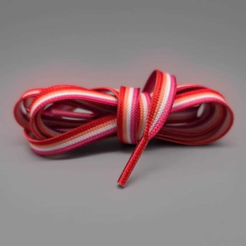 Ein harmonischer Farbverlauf aus kräftigen Orange-, Rosa-, Weiß- und Rottönen zeichnet dieses zu einem Knoten gebundene Paar Schnürsenkel aus. Das textile Accessoire repräsentiert die offizielle Flagge der lesbischen Gemeinschaft auf grauem Untergrund.