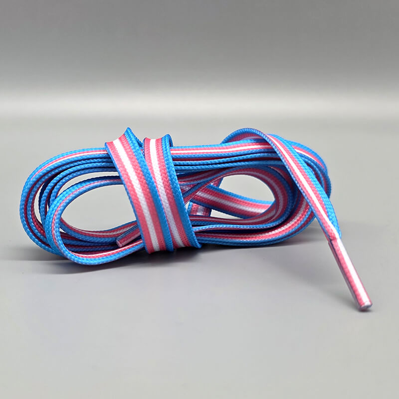 Ein Paar flache Schnürsenkel, ordentlich zusammengerollt, mit abwechselnden Streifen in den Farben der Transgender-Flagge (hellblau, rosa, weiß) und silbernen Metallspitzen auf einem hellgrauen Hintergrund.