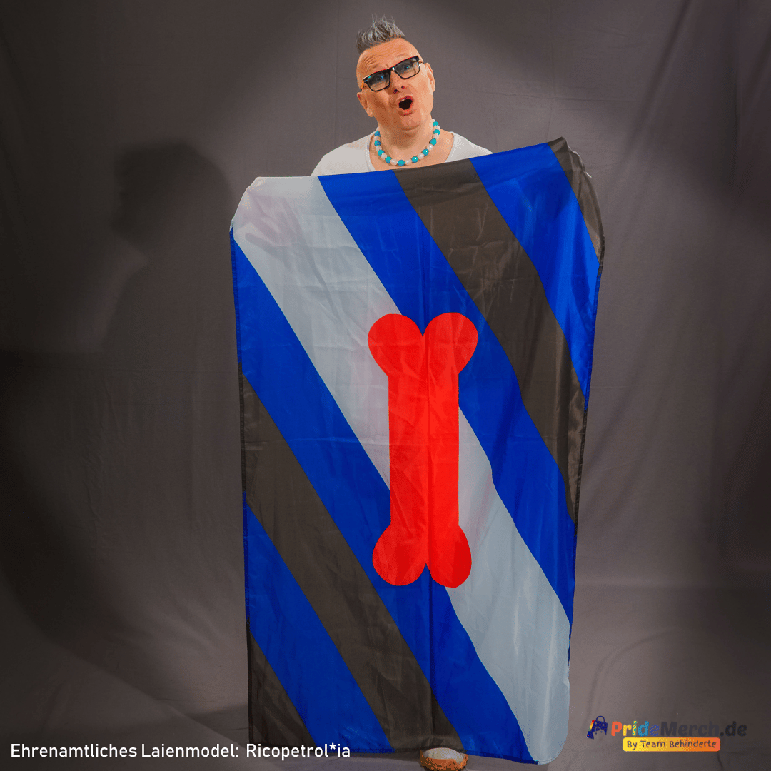 Das ehrenamtliche Laienmodell Ricopetrol*ia hält die Puppy Play Pride Flagge aufrecht stehend vor dem Körper. Die 150x90 cm große Polyester-Fahne verdeckt den Körper frontal und präsentiert das Knochen-Motiv zentriert im Fotostudio.