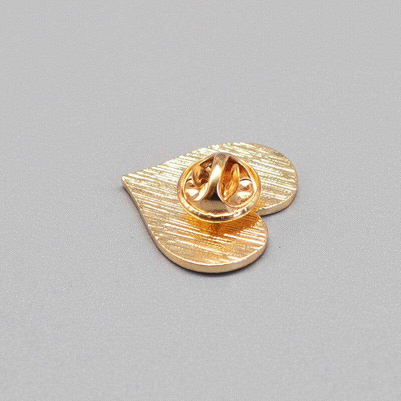 Die detaillierte Rückseite des silbernen Herz-Ansteckers offenbart die spitze Metallnadel mit dem dazugehörigen, abgenommenen Schmetterlingsverschluss. Das flache Schaubild veranschaulicht den sicheren Haltmechanismus für Textilien.