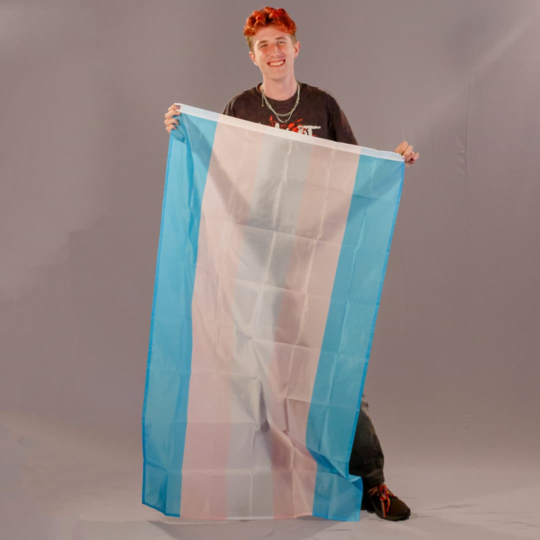 Einer der Initiatoren von PrideLAB, hält die große Trans-Pride-Flagge in 150x90 cm senkrecht vor sich.